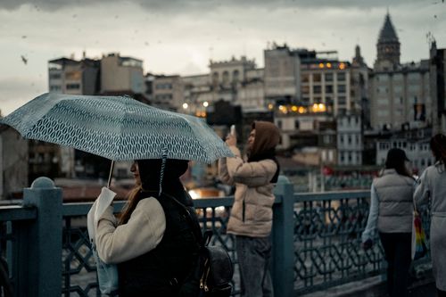 Free A rainy urban scene in Istanbul showcasing the iconic Galata Tower and locals with umbrellas. Stock Photo