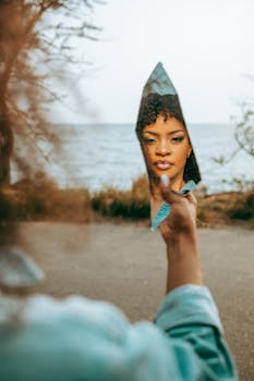 Artistic portrait of a woman reflected in a shard of mirror by the sea.