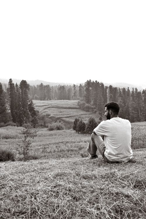 Free A man sitting in peaceful contemplation overlooking a vast rural meadow. Stock Photo