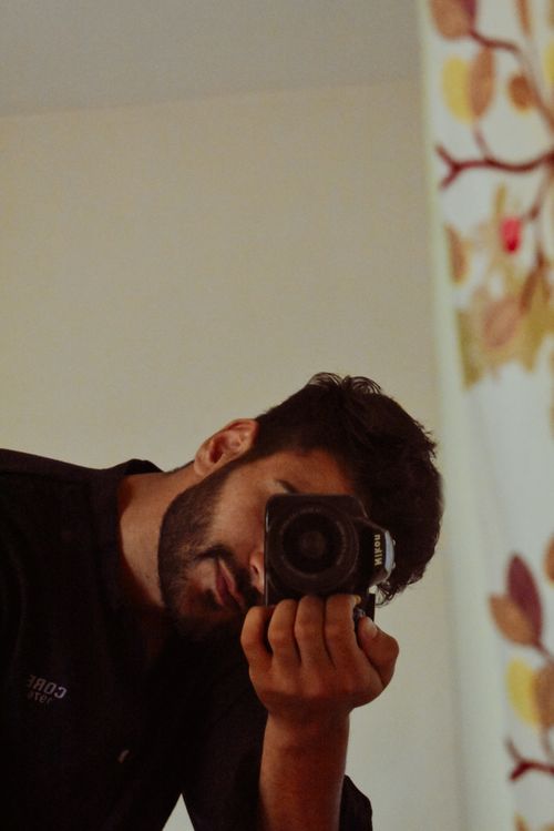 Free Man in black shirt using a DSLR camera, taking a mirror selfie indoors. Stock Photo