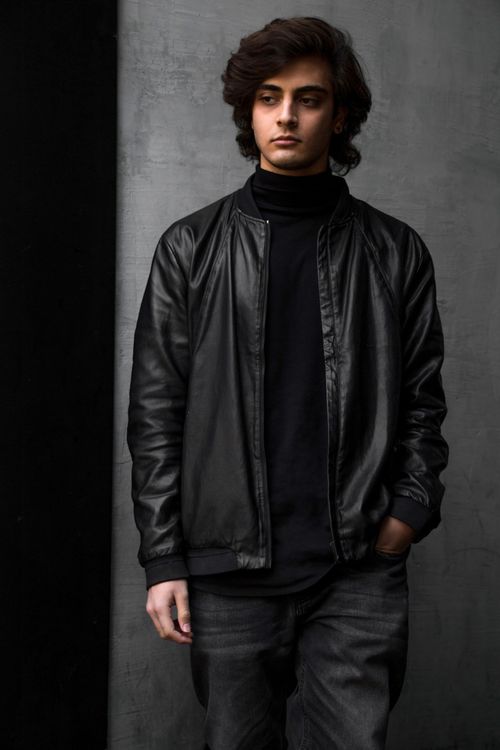Free Stylish young man in a black leather jacket posing against a gray background. Stock Photo