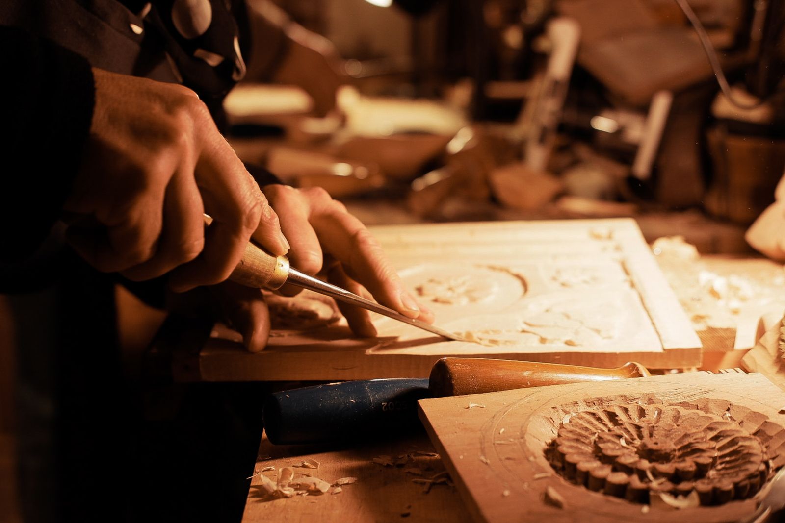 Craftsman skillfully carves intricate designs into wood under warm lighting.