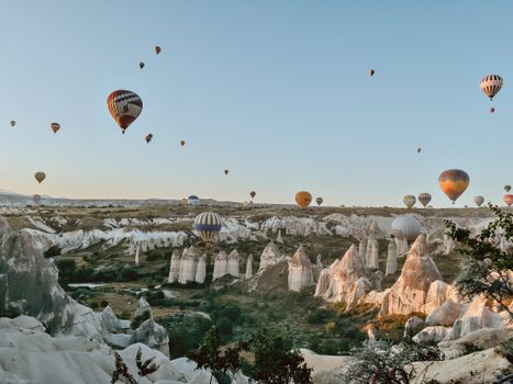 Beautiful hot air balloons soar over the unique rock formations of Cappadocia, Turkey at sunrise.