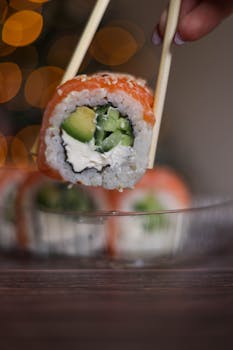 Delicious sushi roll held by chopsticks featuring avocado, salmon, and cream cheese, perfect for Japanese cuisine lovers.