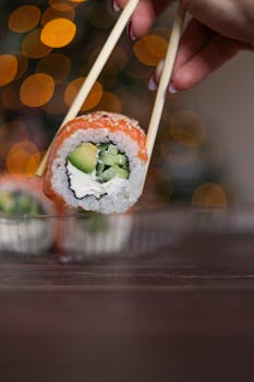 A sushi roll held by chopsticks against a bokeh background.