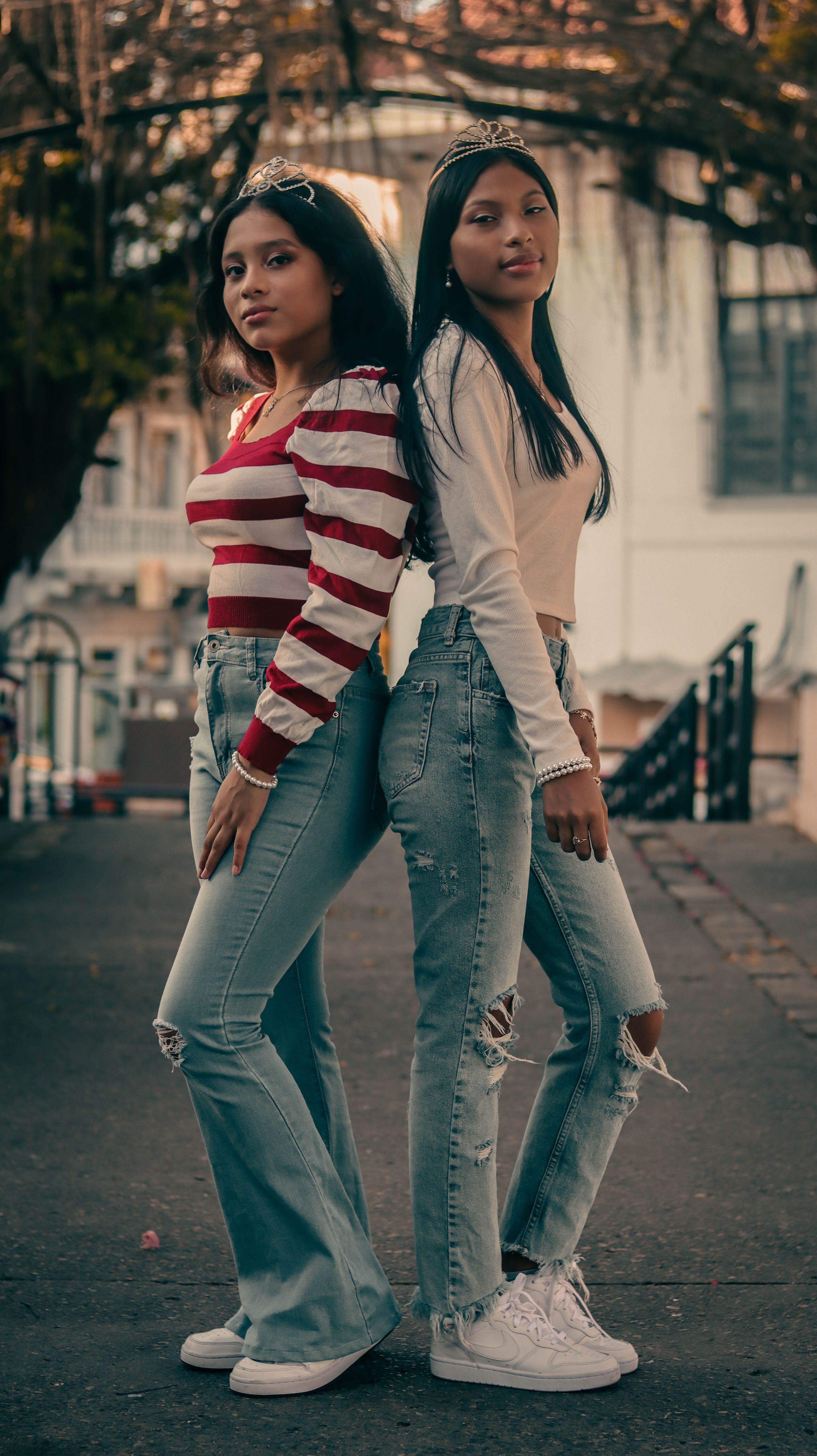 Duas jovens posam em moda casual com jeans rasgado e blusas listradas ao ar livre. Ambiente urbano.