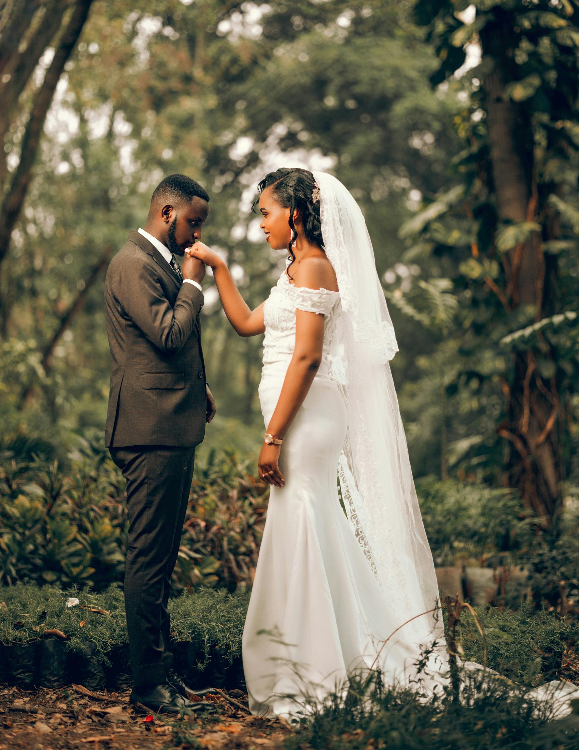 newlyweds standing and kissing hand in forest