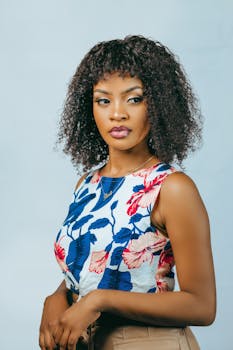 Chic portrait of a young woman with curly hair and a stylish floral top against a white background.