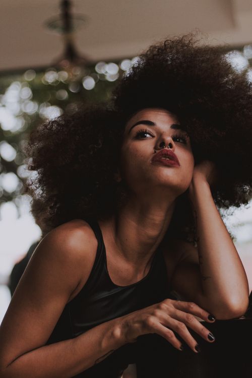 Free Stylish outdoor photoshoot featuring a woman with natural afro hair in a low angle pose. Stock Photo
