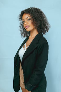 A young woman posing confidently in a black blazer against a light blue background.