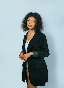 Portrait of a confident young Black woman in a fashionable overcoat against a light background.