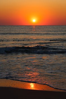 A tranquil beach sunset with vibrant colors reflecting over the calm ocean waves.