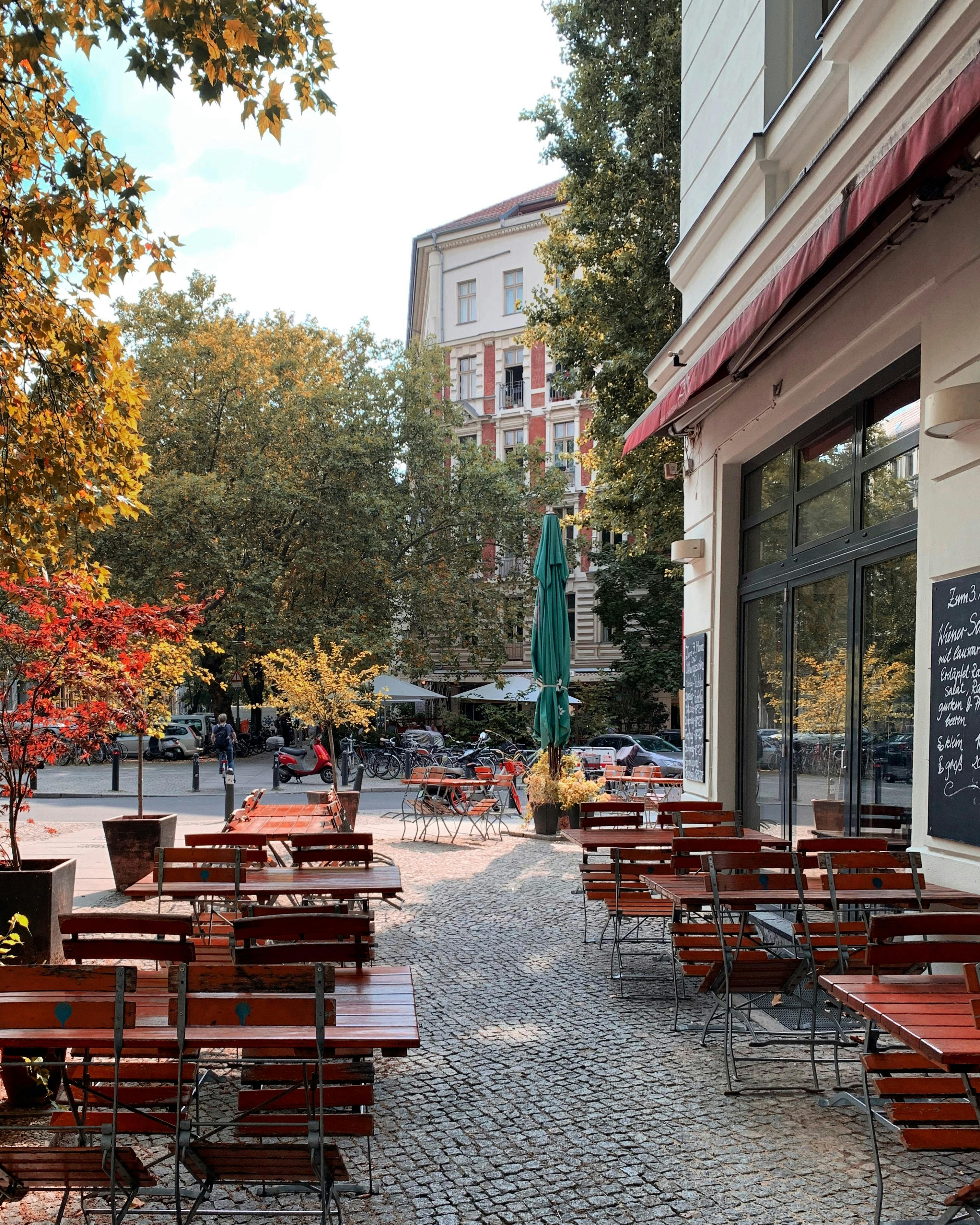 Cozy outdoor cafe scene on a sunny autumn day in Berlin, Germany featuring empty wooden tables and trees.
