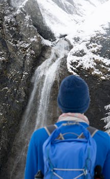 A person in winter attire standing in front of a snowy waterfall in the Austrian Alps.