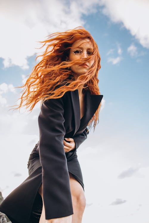 A woman with red hair and long hair is standing on a cliff