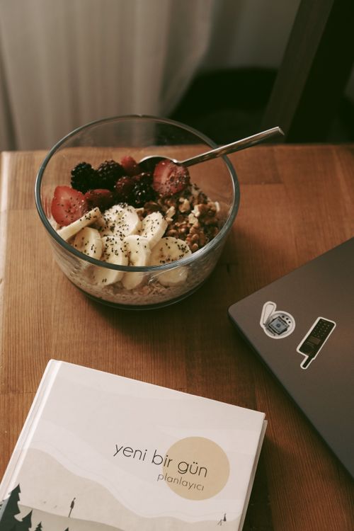 Free A delicious bowl of granola with fruit toppings beside a planner and laptop. Stock Photo
