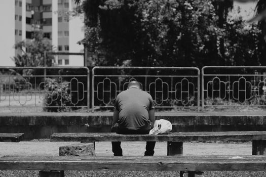 A Man Sitting on a Wooden Bench in Front of an Apartment Building