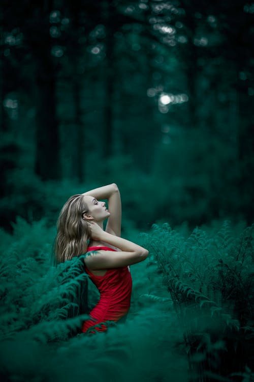 Женщина в красном платье без рукавов, стоя возле листьев папоротника