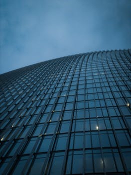 Low-angle view of a modern skyscraper with glass windows and curved design against a cloudy sky.