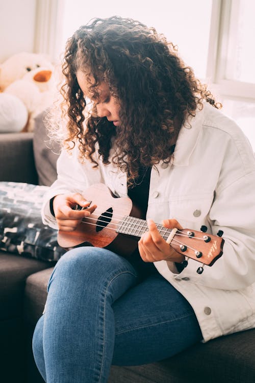 Free Photo of Woman Playing Ukulele White Sitting on Gray Sofa Stock Photo