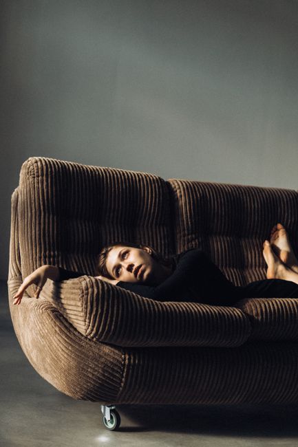 A woman relaxing on a ribbed brown sofa in a modern indoor setting, captured in soft sunlight.