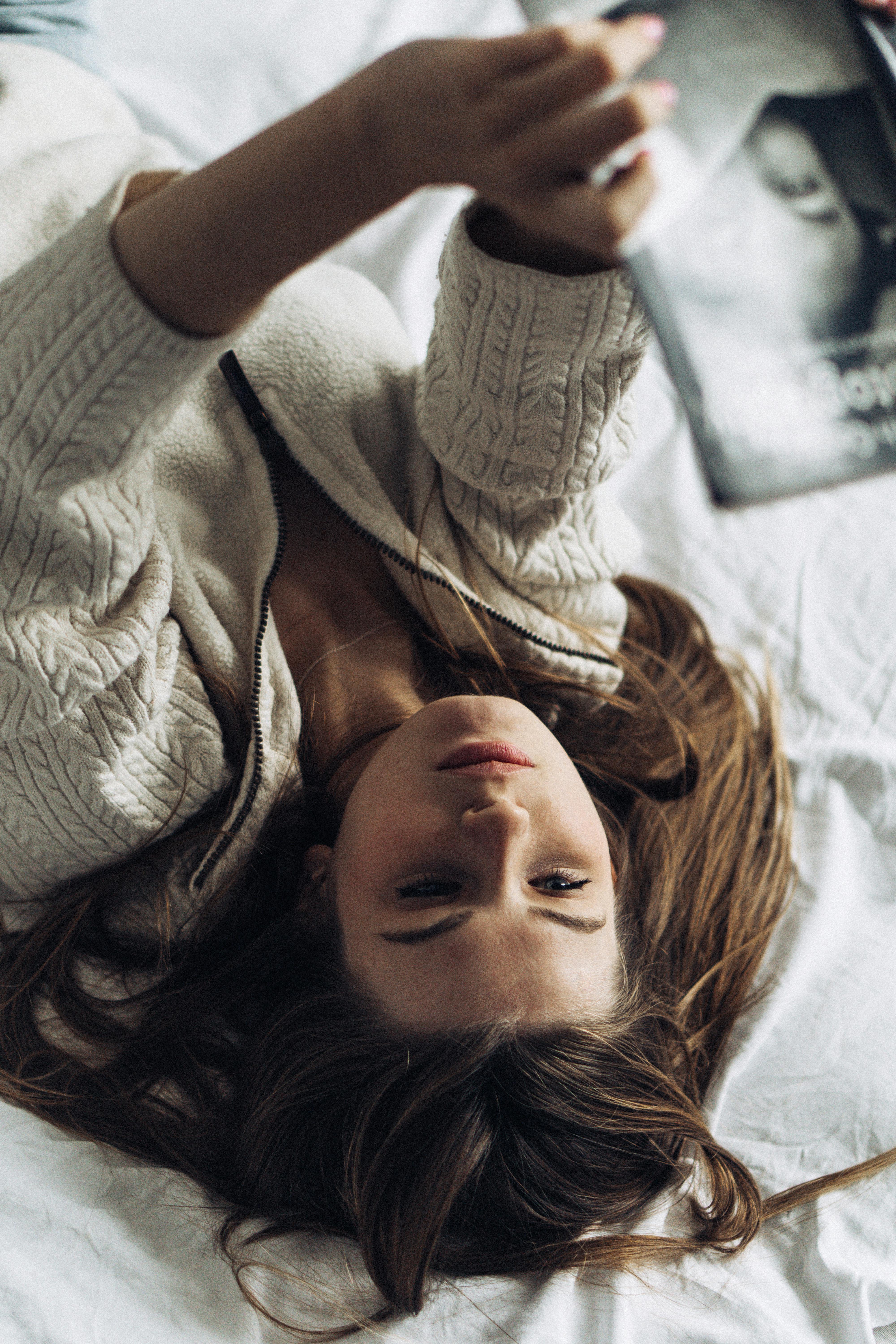 Woman with long brown hair lying on a bed reading a book in a cozy setting.