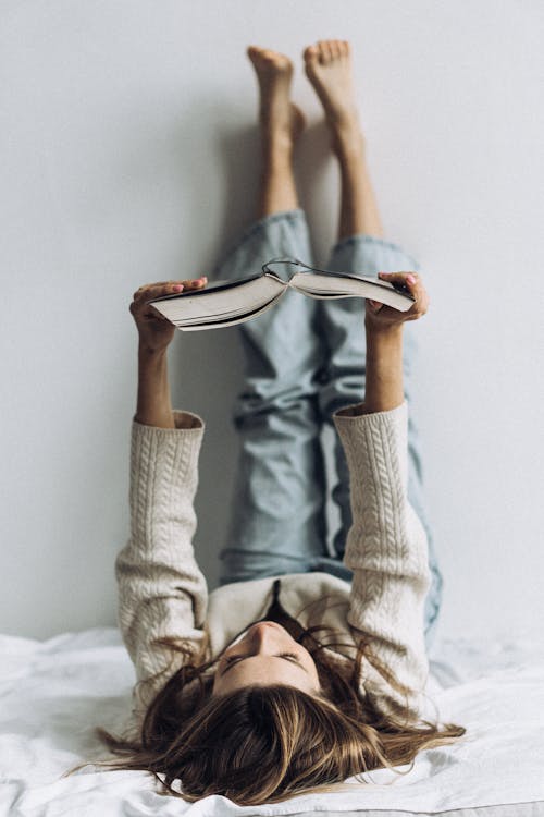 Woman Reading a Book Lying in the Bed With Her Legs Up Against the Wall