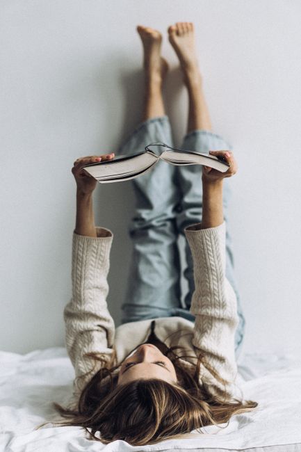 A woman lies in bed with legs up, enjoying a book in a cozy setting.