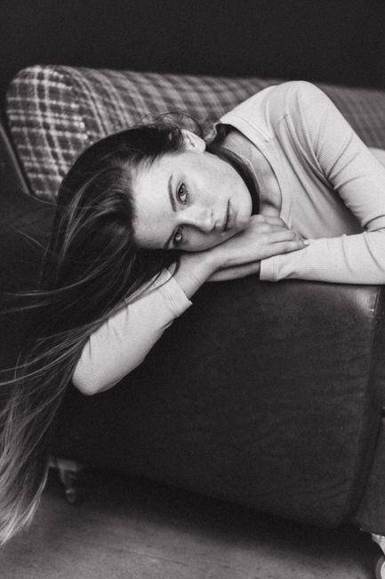 Artistic black and white portrait of a young woman lying on a couch, exuding elegance and poise.