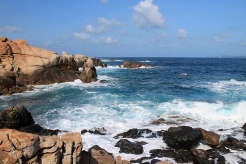 Free Breathtaking rocky coastline with powerful ocean waves crashing against the rocks under a clear blue sky. Stock Photo