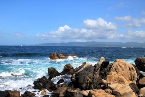 Free Beautiful rocky shore with waves crashing against the coast under a blue sky. Stock Photo