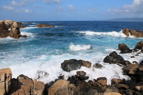 Free Stunning seascape capturing waves crashing on rocky coastline under a bright blue sky. Stock Photo