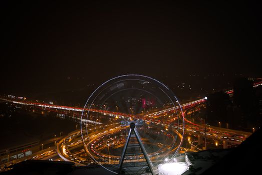 Stunning aerial view of a city at night featuring a glowing Ferris wheel and bustling highway.