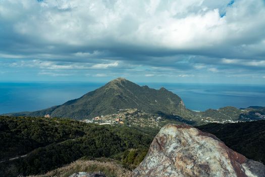 A breathtaking view of a mountain peak with ocean in the background and dramatic clouds overhead.