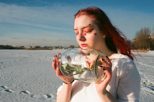 Женщина, держащая прозрачную стеклянную бутылку с розой внутри