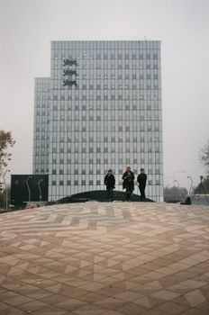 当代城市场景中，光滑的摩天大楼立面和图案人行道上站着三个人