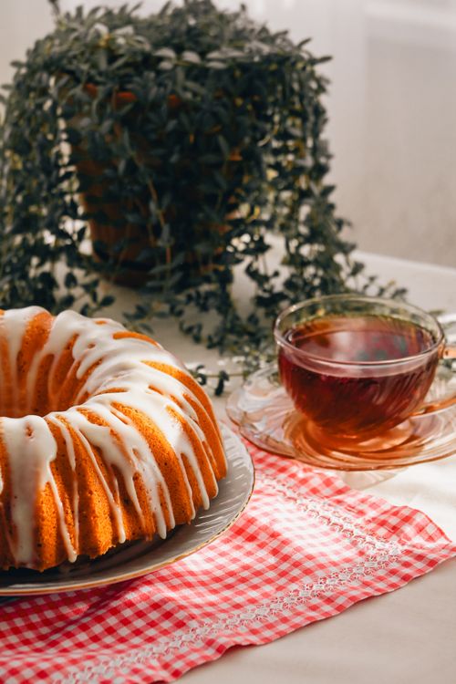 Free Close-up of a delicious iced bundt cake with a cup of tea and a green plant in the background. Stock Photo