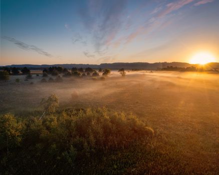 Golden sunrise over misty fields in West Newton, MN, showcasing tranquil countryside beauty.