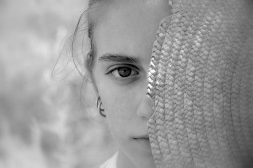 Free Close-up black and white portrait of a young woman partially hidden behind a straw hat. Stock Photo