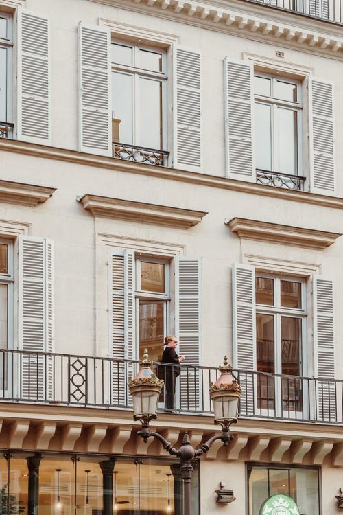 Free Classic building facade with balcony and shutters, featuring a person enjoying city views. Stock Photo