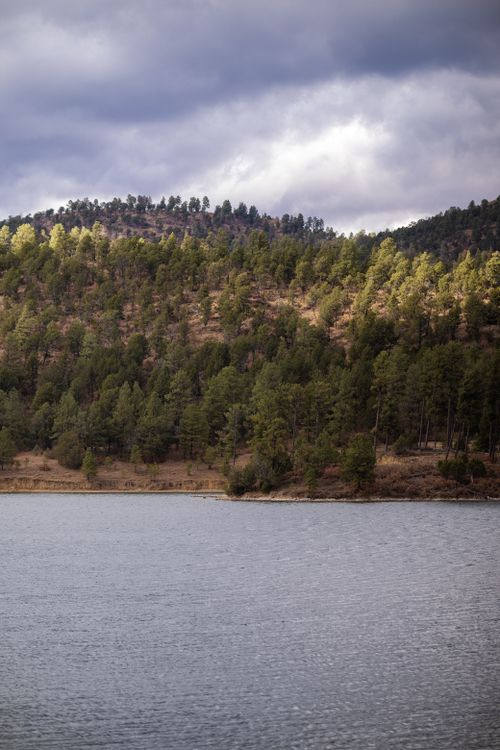 Free Tranquil lake view with forested hills under a cloudy sky in Ruidoso, New Mexico. Stock Photo