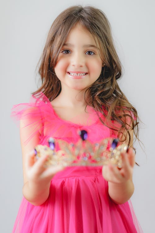 A Little Girl in a Pink Dress Holding a Tiara 