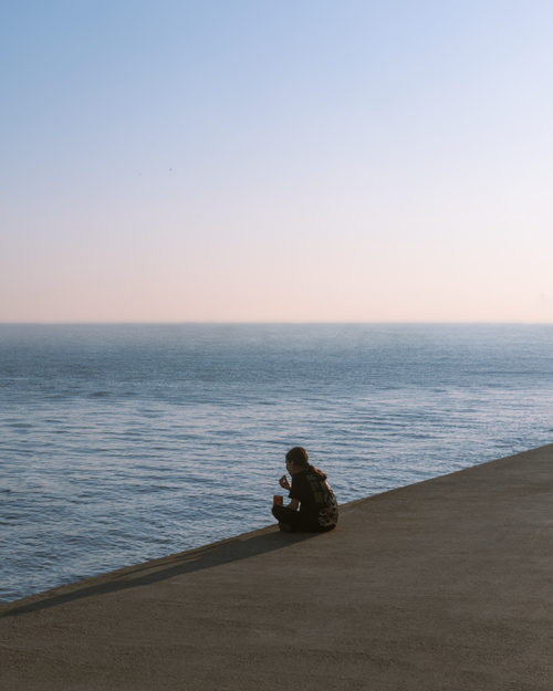 Free A person sits alone by the sea at dusk, embracing solitude and peace. Stock Photo
