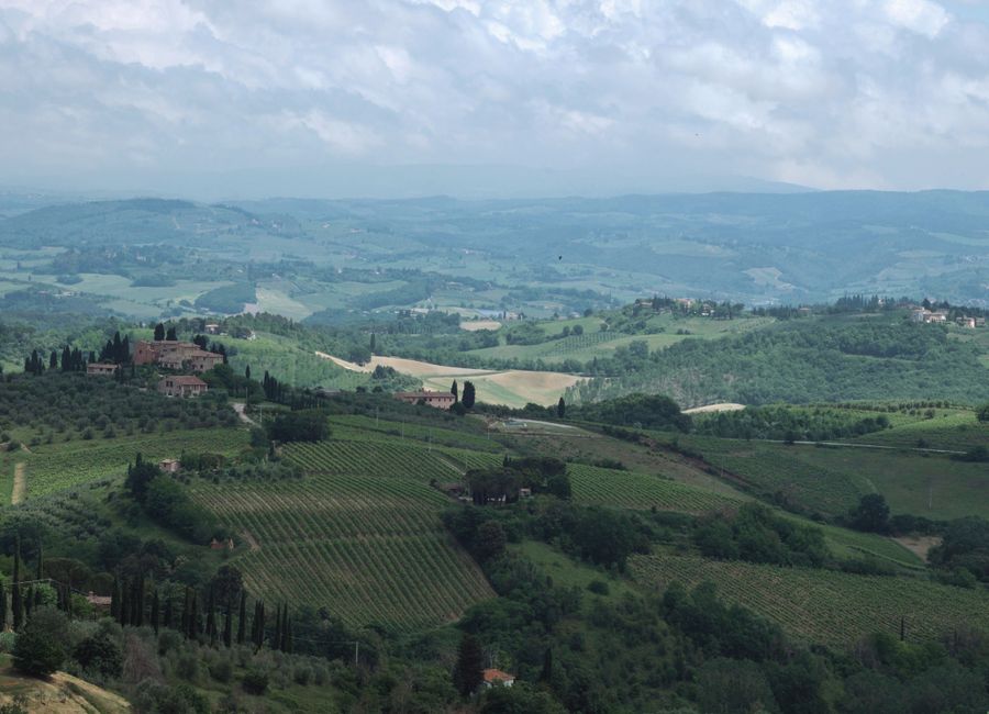 Stunning aerial shot of Tuscany's rural landscape with vineyards and rolling hills under a cloudy sky.