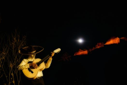 A man in a mexican costume playing guitar in the moonlight