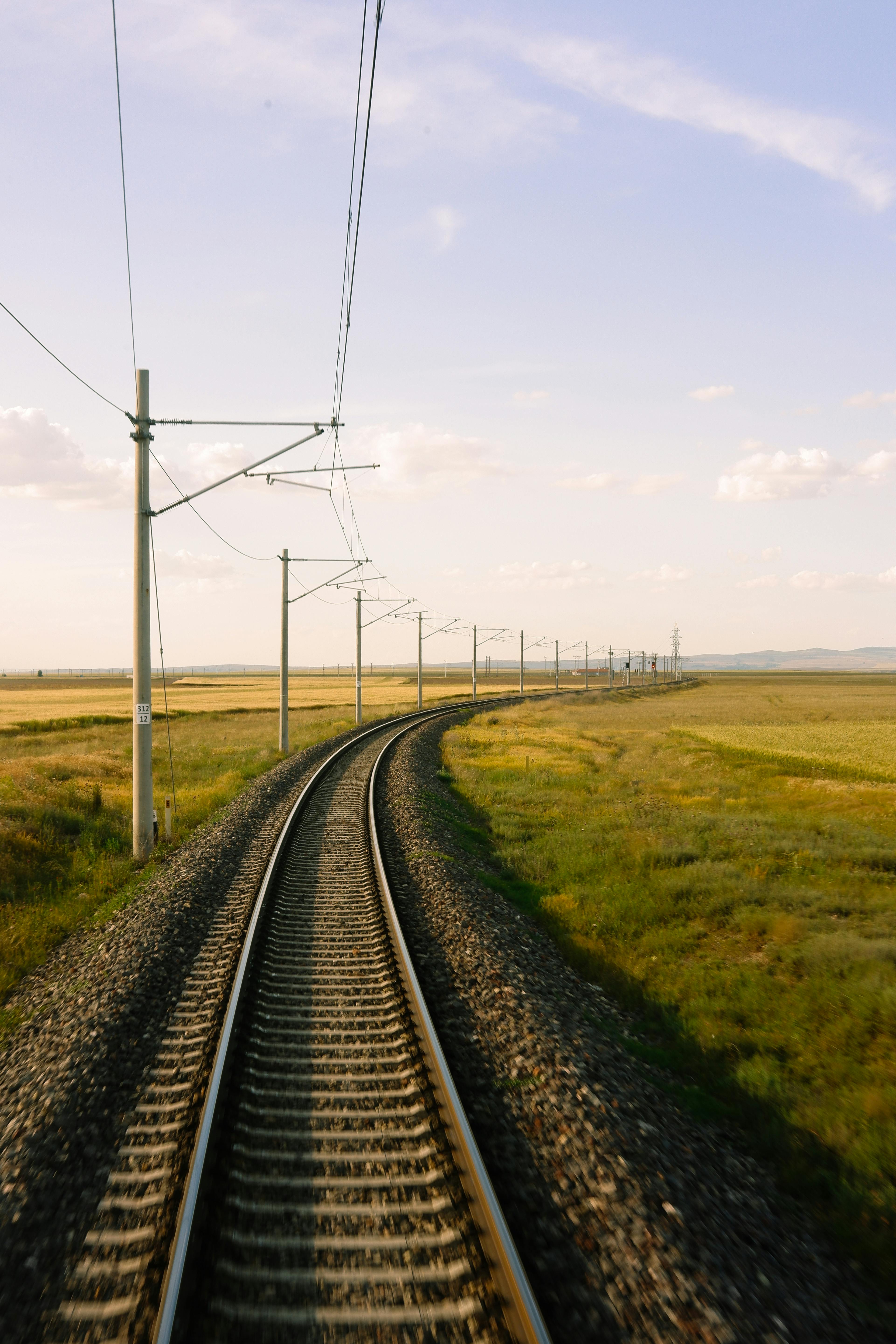 Railway tracks curve through the serene countryside under a clear blue sky, showcasing rural tranquility.