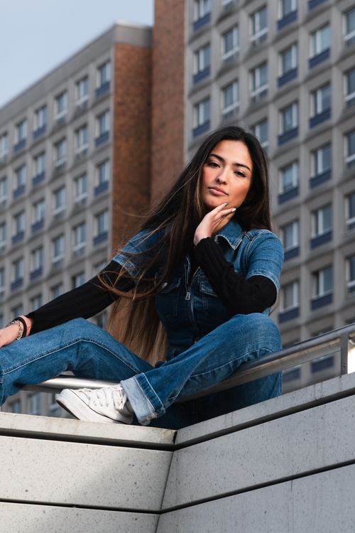 Free Confident woman in denim seated on a rooftop with city backdrop, showcasing urban style. Stock Photo
