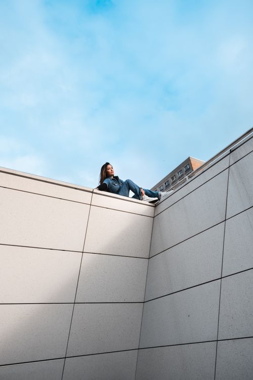 Free Woman sitting on a modern building corner in an urban setting under a clear sky. Stock Photo