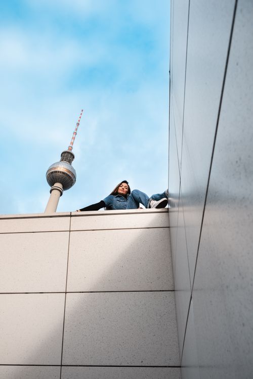Free Low angle view of a woman sitting near the iconic Berlin TV Tower on a sunny day. Stock Photo