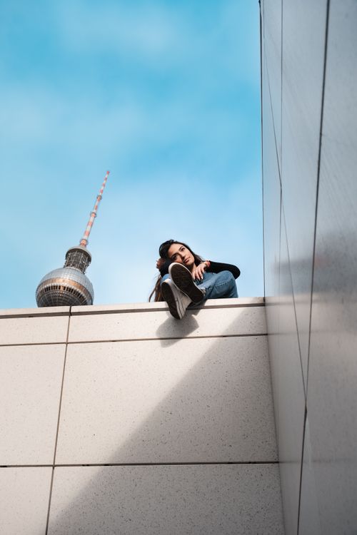 Free A young woman sits on a rooftop with Berlin's TV Tower in the background. Urban, modern vibe. Stock Photo